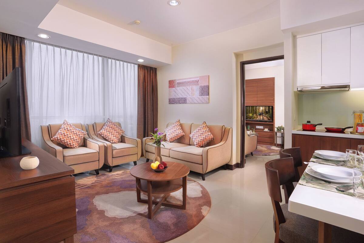 A modern living room with a sofa set, a coffee table with fruit, and a dining area with a table set for two.