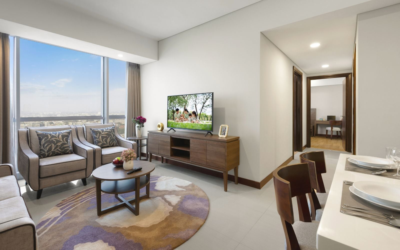 Una sala moderna con un televisor de pantalla plana, una zona de comedor con una mesa dispuesta para dos personas y un amplio ventanal con vistas a la ciudad.