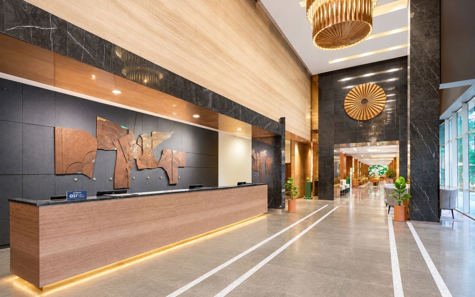 A modern hotel lobby with a reception desk, a large wall art piece, and a circular decorative element on the wall.