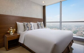 A hotel room with a large bed, a nightstand with a vase of flowers, and a city view through large windows. - Somerset Kencana Jakarta (Jakarta)