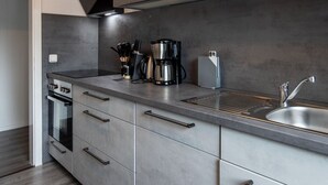 A modern kitchen with grey cabinetry, a stainless steel sink, and a built-in oven. - Ferienwohnung Watt, Modern und Liebevoll Eingerichtet, Wlan, Smart TV (Wilhelmshaven)