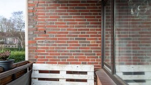 A balcony with a brick wall, wooden steps, and a white wooden bench. - Ferienwohnung Watt, Modern und Liebevoll Eingerichtet, Wlan, Smart TV (Wilhelmshaven)