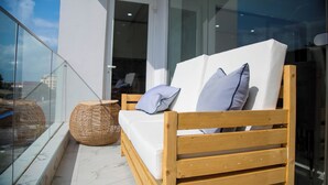 A wooden bench with cushions and a woven basket on a balcony with a glass railing. - MiVi (Lagos)
