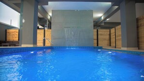 An indoor swimming pool with clear water, a wooden deck area, and a modern architectural design. - MiVi (Lagos)