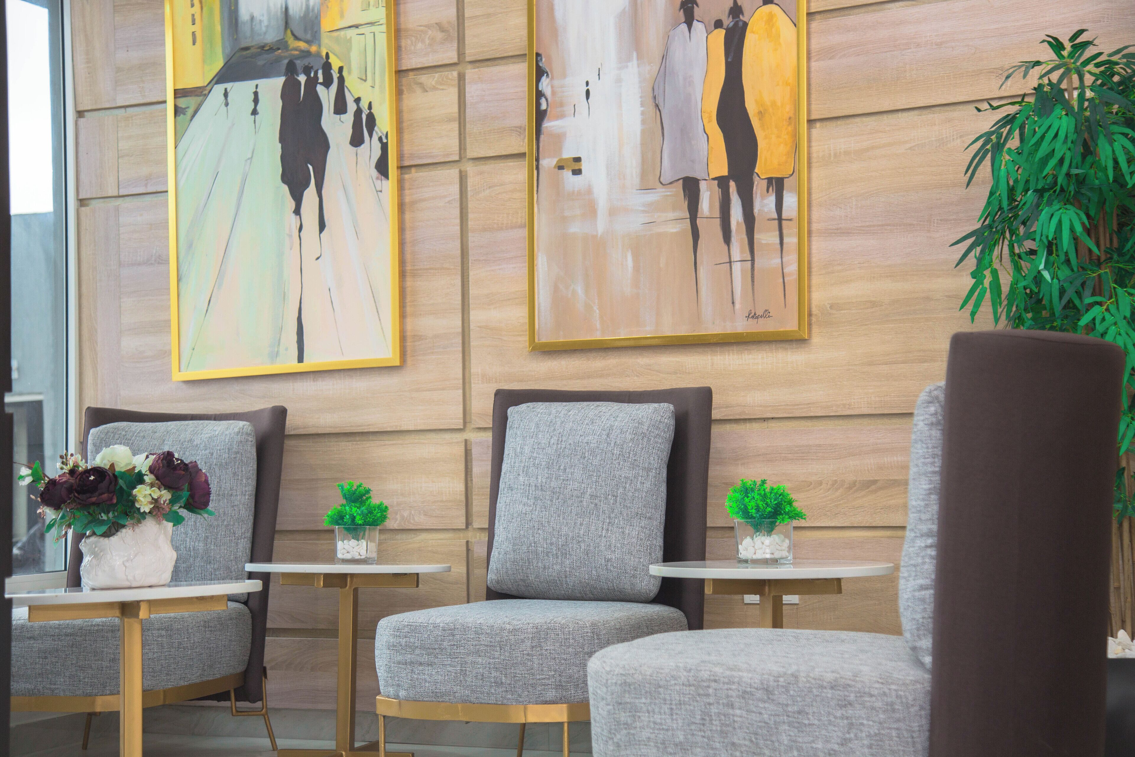 A modern lobby with grey upholstered chairs, small tables with potted plants, and two large abstract paintings on the wall.