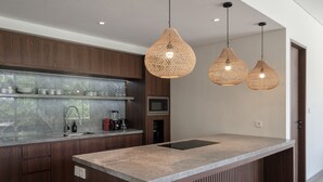 A modern kitchen with wooden cabinets, a marble countertop, and three woven pendant lights. - Villa Jenggala by GORO (Ubud)