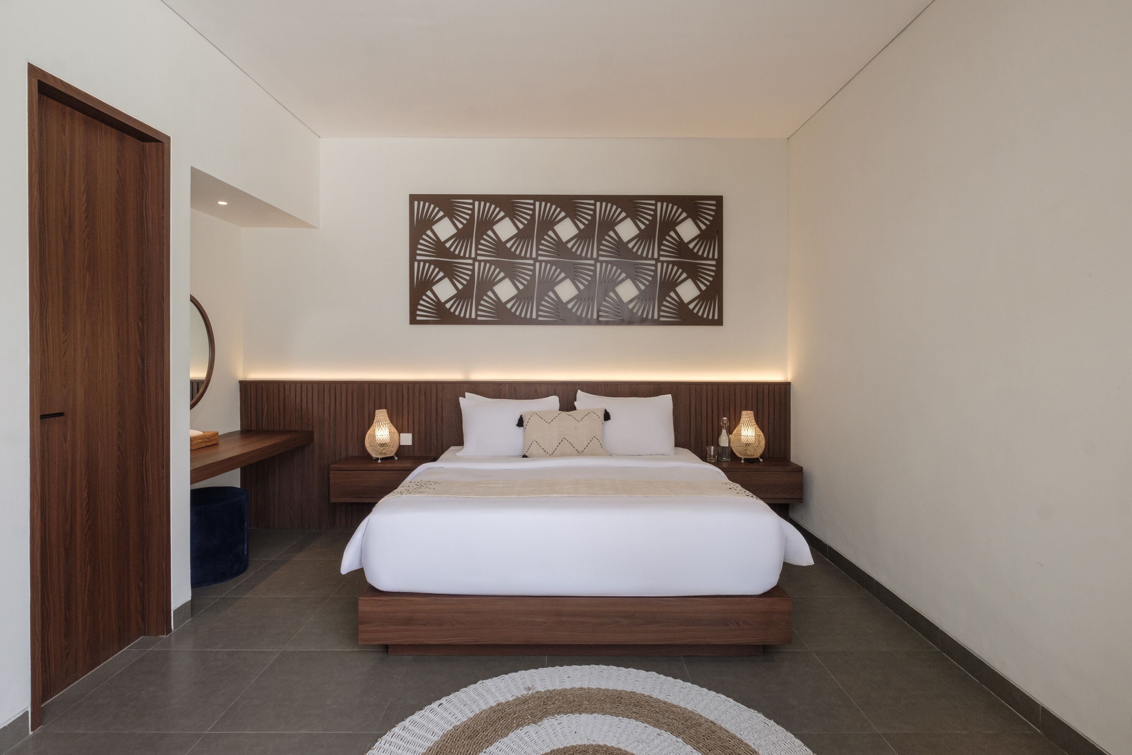 A modern bedroom with a large bed, wooden headboard, bedside lamps, and a decorative wall piece.