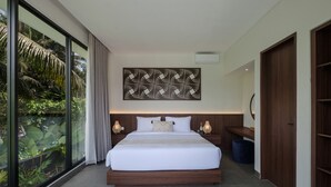 A modern bedroom with a large bed, a view of greenery through floor-to-ceiling windows, a decorative wall piece, and a wooden wardrobe. - Villa Jenggala by GORO (Ubud)