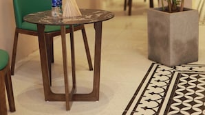 Een ronde tafel met een rieten mand, twee waterflessen en een groene stoel in een kamer met betegelde vloer en een bloempot.