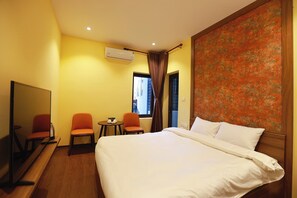 A hotel room with a large bed, two orange chairs, a small table, a TV, and an air conditioning unit. - Le Grand Hotel - by Bay Luxury (Hanoi)