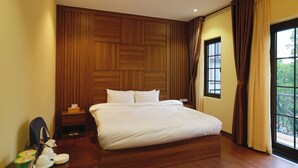 Een hotelkamer met een groot bed, houten lambrisering aan de muur, een nachtkastje en een raam met gordijnen.