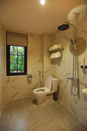 A bathroom with a toilet, a shower, a window with a view, and marble walls. - Le Grand Hotel - by Bay Luxury (Hanoi)