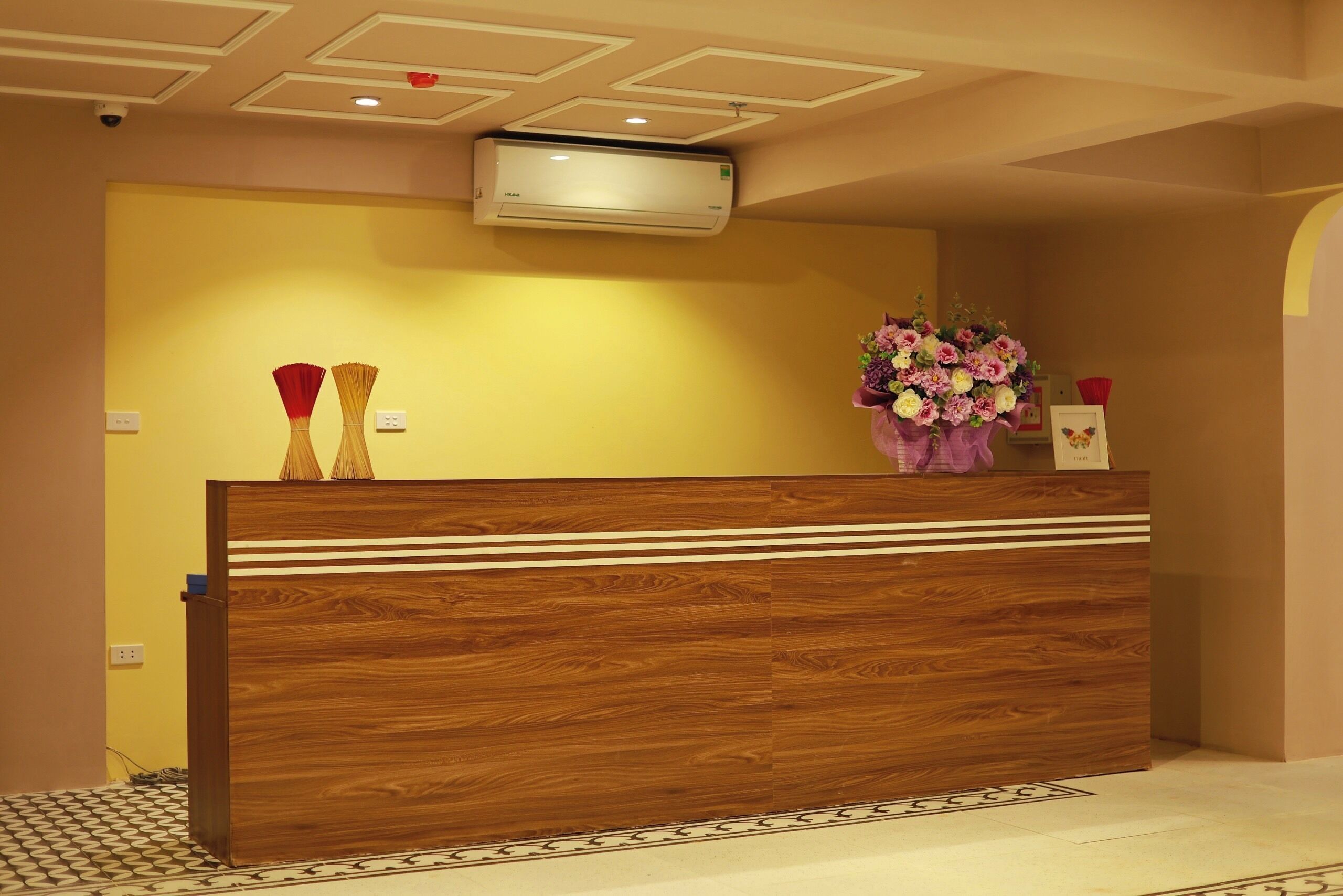 A reception desk with a wooden finish, a wall-mounted air conditioner, and a floral arrangement.