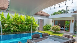 A poolside area with a glass-top table and wicker chairs, surrounded by lush greenery and a tiled pool. - Tranquil Escape: Private 4BR Pool Villa with Garden (Rawai)