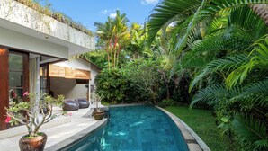 A modern pool area with a clear blue pool, surrounded by lush greenery and a contemporary building with large windows.