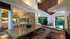 A modern kitchen with a wooden dining table, built-in appliances, and a view of a lush garden and pool.