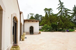 Un patio con entrada a un edificio, jarrones grandes y mobiliario exterior.