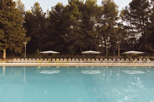 Piscina con sillones de descanso y sombrillas, rodeada de árboles.