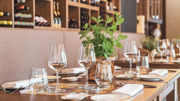 A restaurant table set with wine glasses, plates, and cutlery, with a potted plant in the center. - Wine & Resort Le Vigne al Castello (Andria)