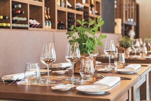 Mesa de restaurante dispuesta con copas de vino, platos y cubiertos, con una planta en maceta en el centro.