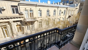 Ein Balkon mit Fliesenboden, einem schwarzen Metallgeländer und Blick auf umliegende Gebäude.
