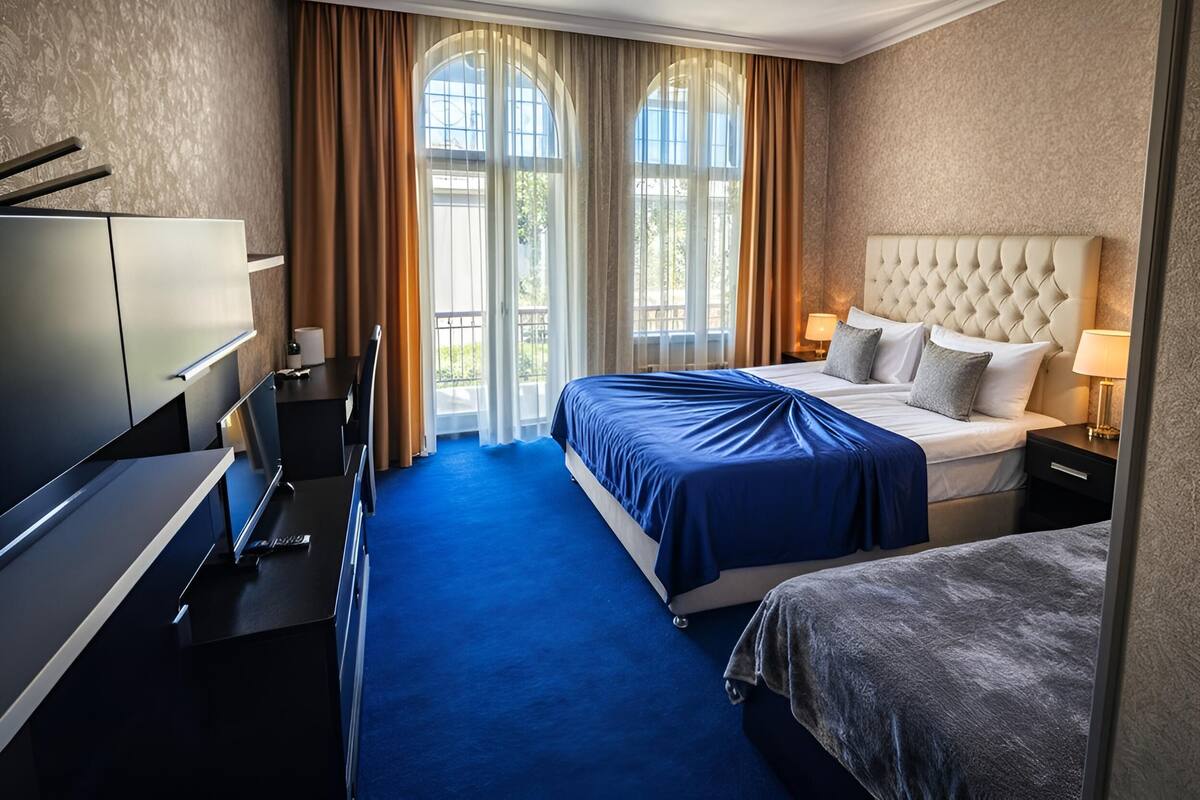 Una habitación de hotel con cama, escritorio, silla, armario y ventana con cortinas.