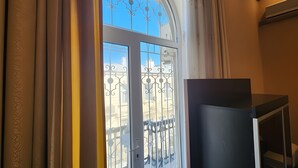 Ein Zimmer mit einem großen Bogenfenster, einem schwarzen Schrank und Blick auf Gebäude.