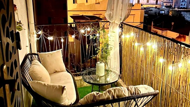 A balcony with a hanging chair, a small table with a plant, and string lights.