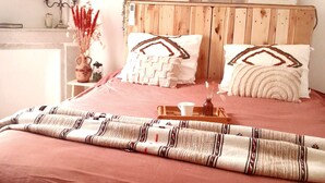 A bedroom with a wooden headboard, two pillows with geometric patterns, a bedside table with a vase and candle, and a framed picture on the wall.