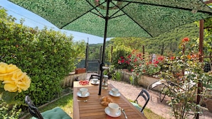A wooden table with white cups and saucers, a green umbrella, and a metal pitcher. - Trekking Home La Via degli Dei Toscana (Vaglia)