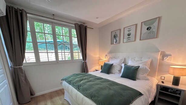 Ein Schlafzimmer mit einem großen Bett, zwei Nachttischen, einem Fenster mit Vorhängen und Wandbildern.