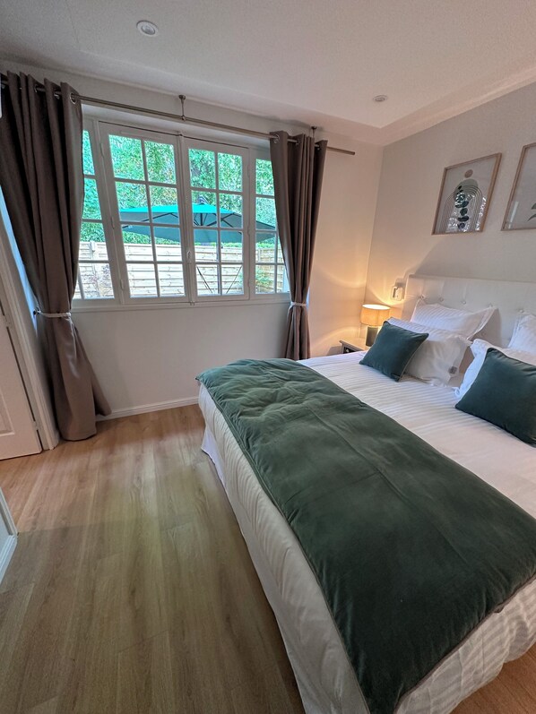Une chambre à coucher avec un grand lit, une fenêtre avec des rideaux, une table de chevet avec une lampe et des œuvres d’art encadrées accrochées au mur.