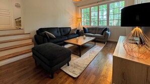 Ein modernes Wohnzimmer mit einer schwarzen Couch, einem Holztisch und einer geometrischen Lampe.