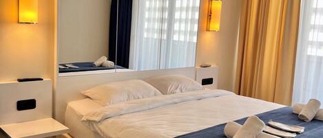 Una habitación de hotel moderna con una cama grande, mesitas de noche, un espejo y un aire acondicionado instalado en el techo.