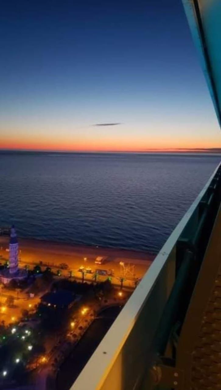 A view of a coastal area at dusk with a lighthouse and illuminated buildings.