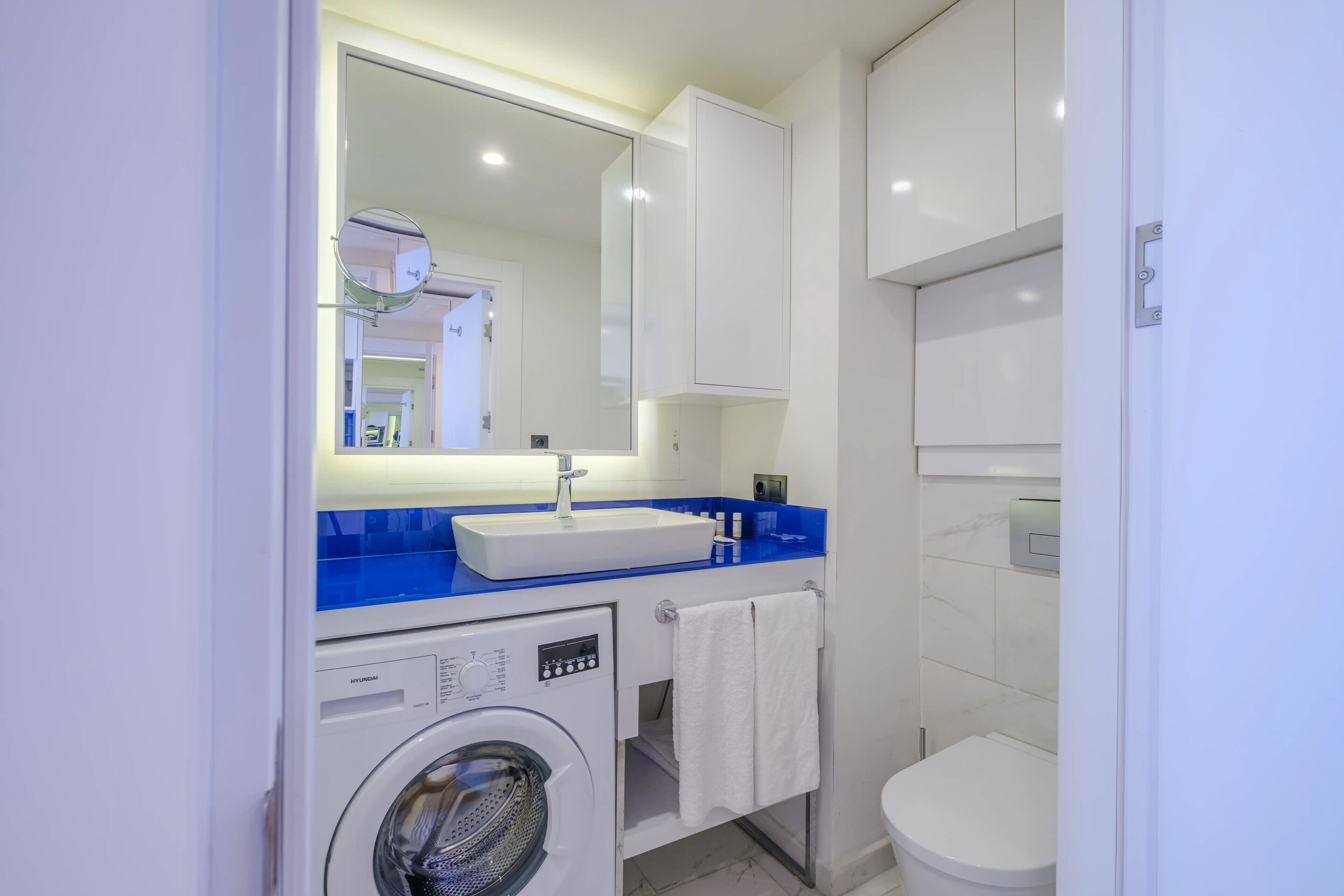 A modern bathroom with a washing machine, a sink, and a toilet.