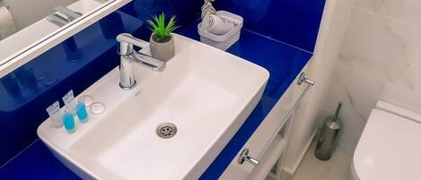 A bathroom with a white sink, blue countertop, and a mirror. There is a small plant on the sink, a toothbrush holder, and a towel rack.