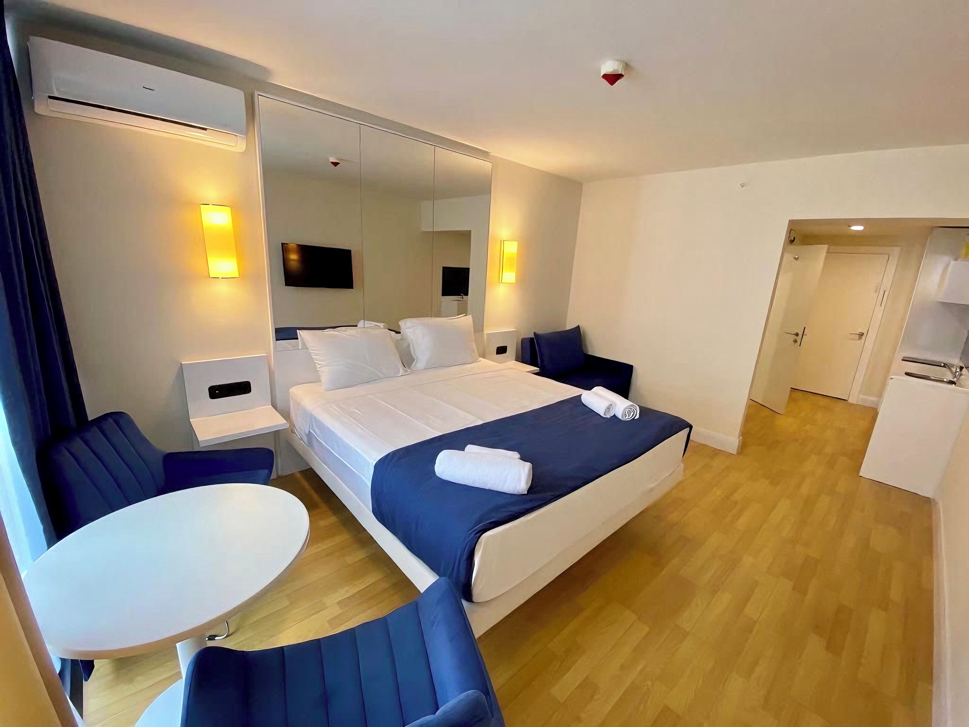 A modern hotel room with a large bed, a desk, a chair, a small table, and a TV.