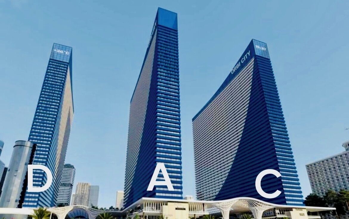 Three high-rise buildings with the letters 'D', 'A', and 'C' prominently displayed on their facades.