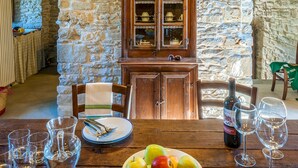 A rustic stone-walled room with a wooden dining table set for two, featuring a plate of fruit, wine glasses, and a bottle of wine. - Casa del Mandorlo 8 Emma Villas (Mercatello sul Metauro)