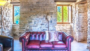 A stone-walled room with a leather sofa, a table with a cloth and sunglasses, and a window with a view of greenery. - Casa del Mandorlo 8 Emma Villas (Mercatello sul Metauro)