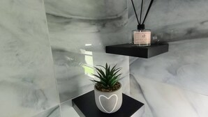 A bathroom with marble walls, a potted plant on a black shelf, and a bottle of perfume on another shelf.