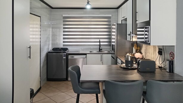 A compact kitchen with a dining area, featuring a refrigerator, stove, sink, and modern appliances.