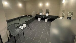 A modern bathroom with multiple showerheads, a seating area, and a large mirror. - Hotel Crystal Plaza (Hitachinaka)