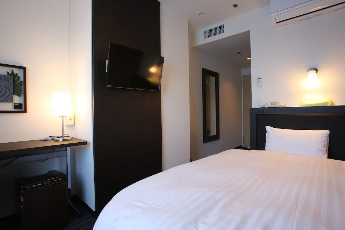 Ein Hotelzimmer mit Bett, Schreibtisch mit Lampe, Flachbildfernseher, Spiegel und Klimaanlage.