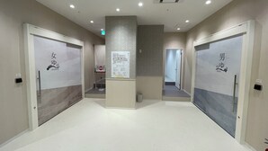 A clean, modern hallway with two doors labeled for women and men, a directional sign, and a trash can. - Hotel Crystal Plaza (Hitachinaka)