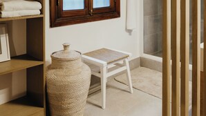 A bathroom with a wooden vanity, a white chair, a large woven basket, and a shower area. - Villa Zebra Moon by muse villas (Cap Malheureux)
