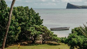 A coastal landscape with a boat, palm trees, and a grassy area. - Villa Zebra Moon by muse villas (Cap Malheureux)