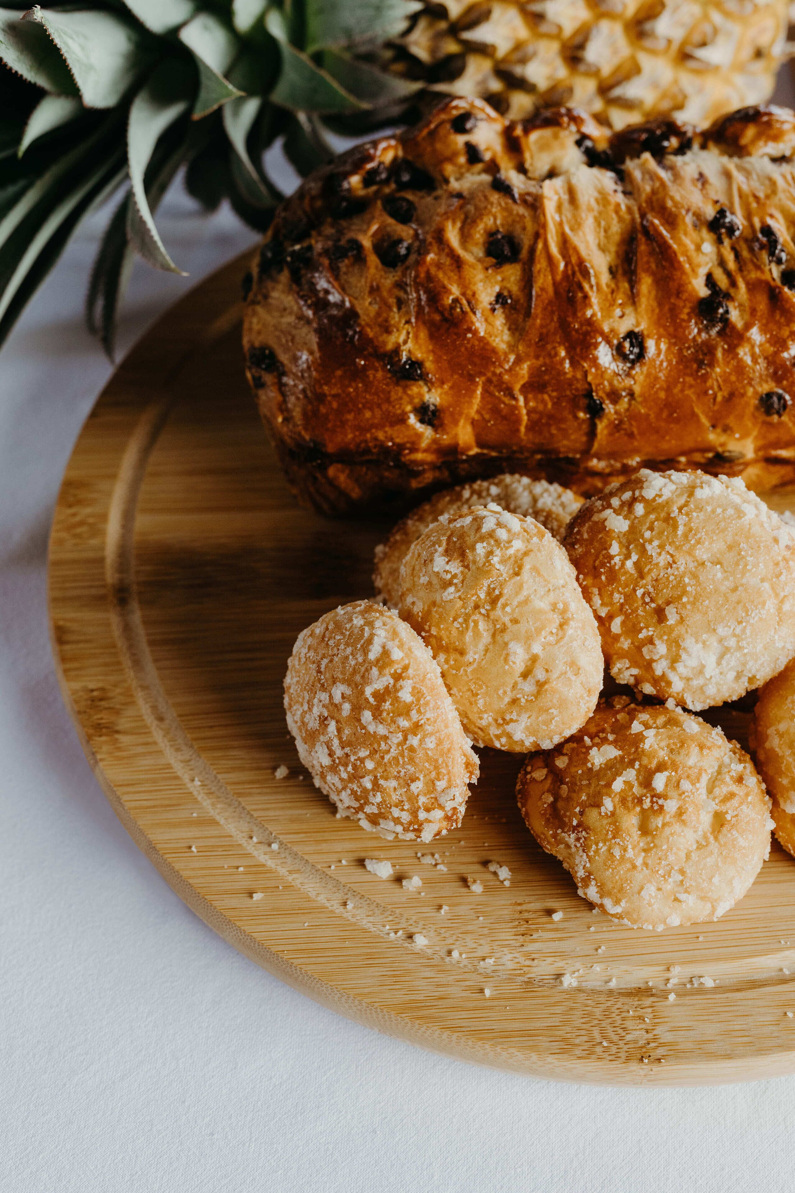 A wooden board with a loaf of bread and several round pastries.