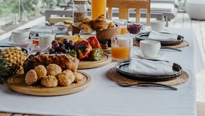 A breakfast table with tropical fruits, pastries, and beverages, overlooking a beach and palm trees. - Villa Zebra Moon by muse villas (Cap Malheureux)